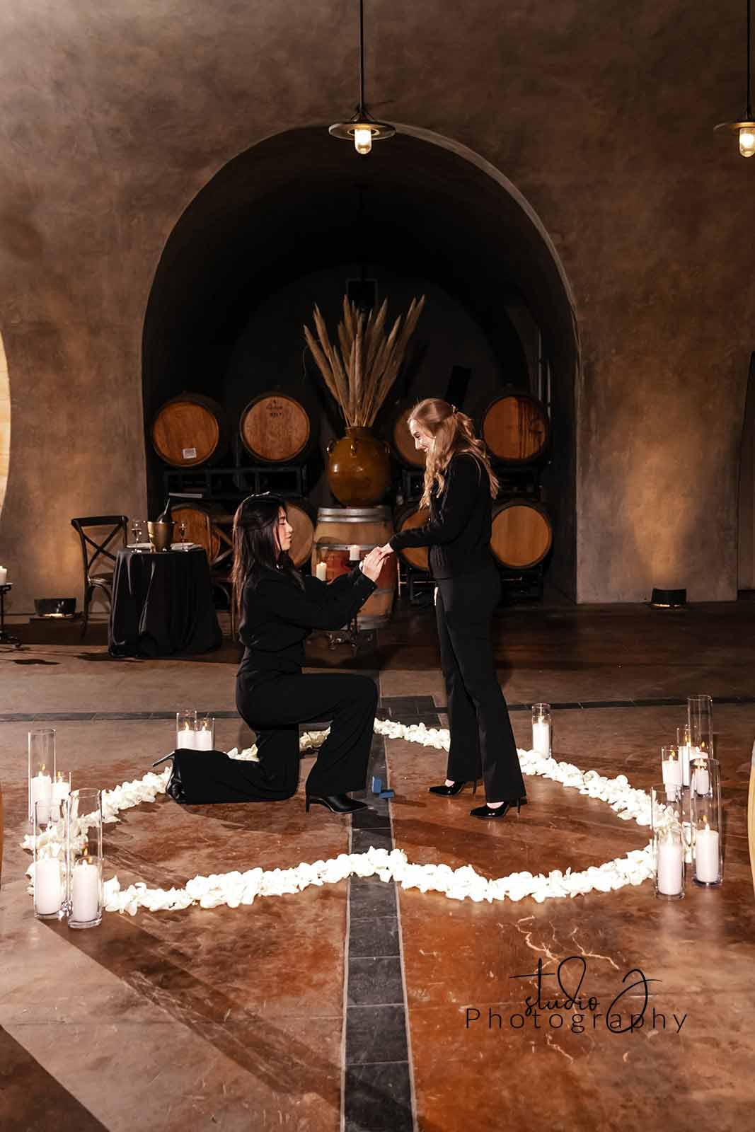 A woman proposes to her love in the Barrel Room of Viansa Winery surrounded by candles and white rose petals. Proposal planned by Blissful Events. Photo by Studio J Photography.